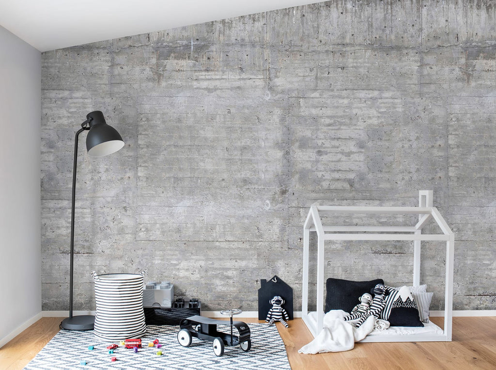 A modern minimalist room featuring a white bed frame, a tall black floor lamp, and children’s toys scattered on a patterned area rug. The room is adorned by a Concrete Grey wallpaper.