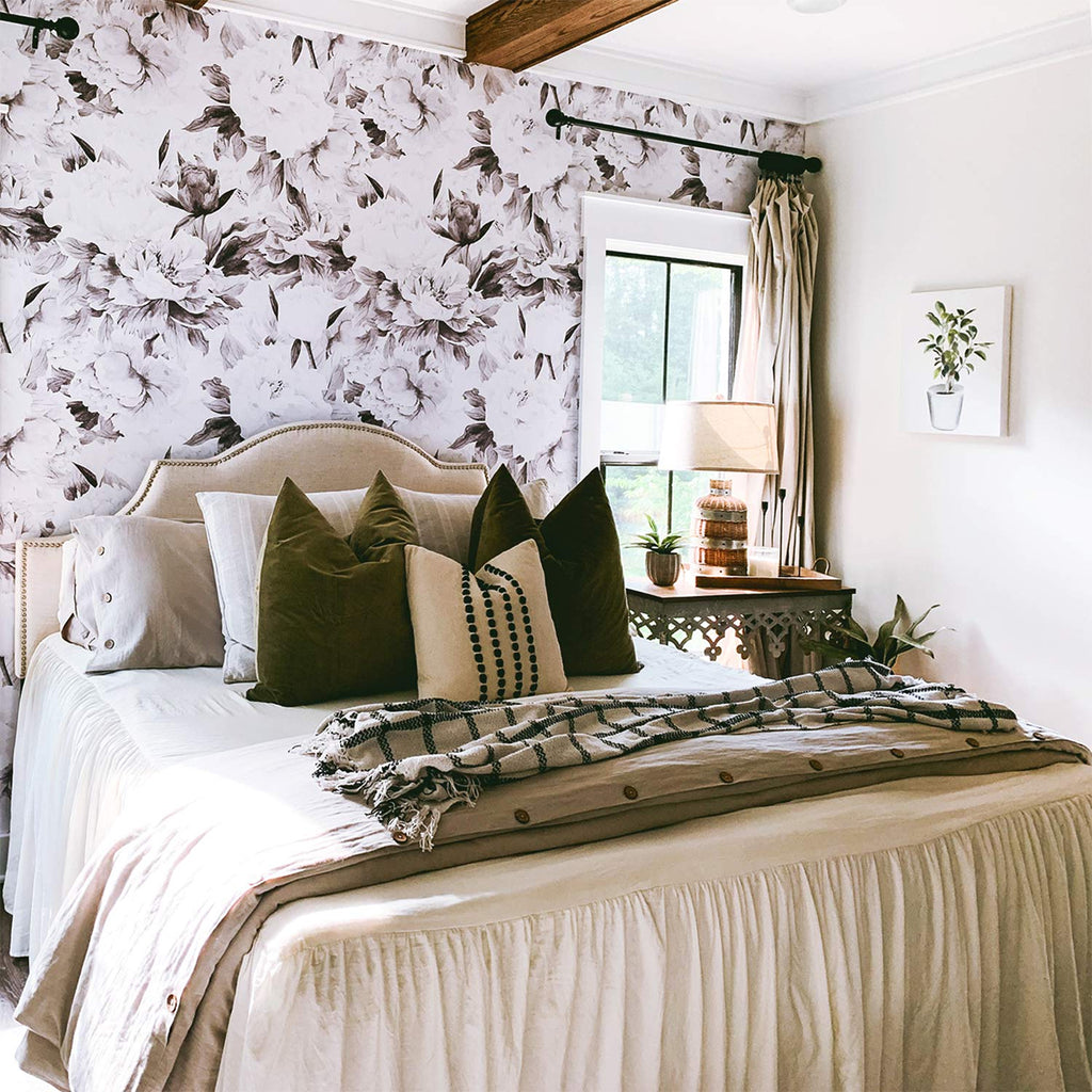 A cozy bedroom with ‘Delicate Grey Peonies, Floral Pattern Wallpaper’, a neatly made bed with plush pillows, wooden accents, and a window revealing greenery. A framed artwork enhance the room’s decor