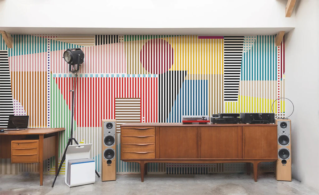 A lively room featuring Diablo, Geometric Wallpaper with colorful striped patterns, vintage furniture, and modern audio equipment creating a dynamic contrast.