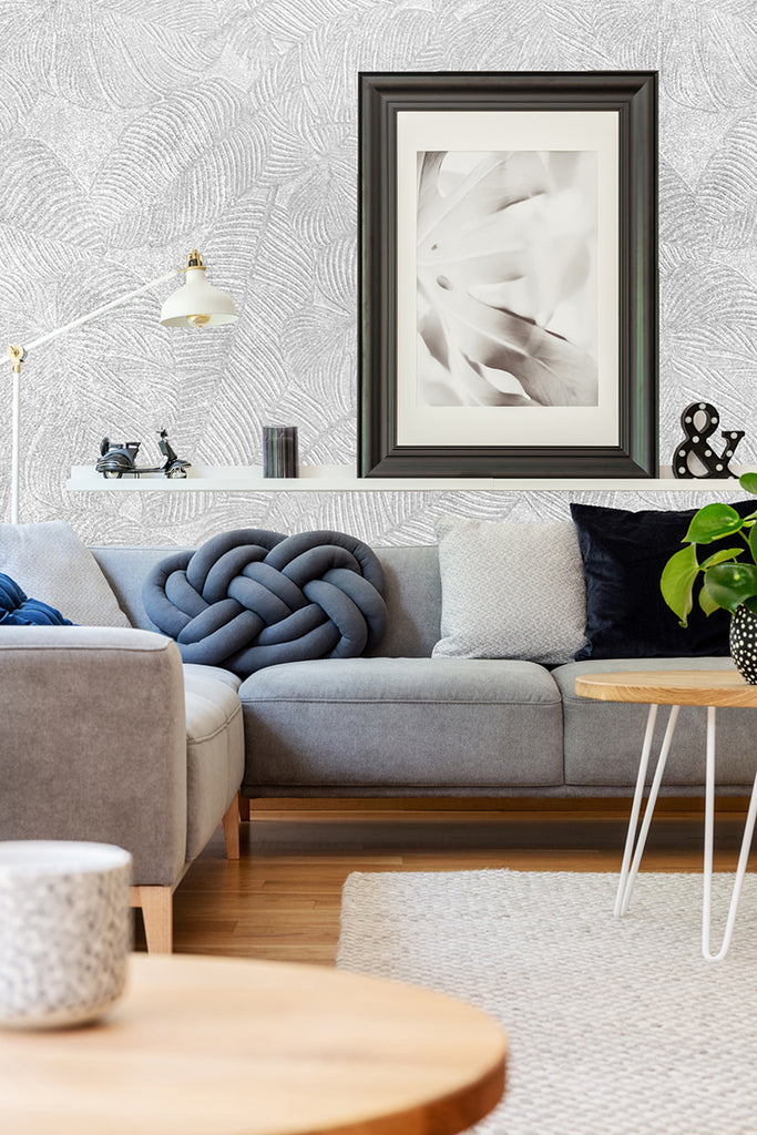 Cozy living room featuring Erin Stone Foliage, Faux Texture Wallpaper with a leafy pattern. The room includes a grey sofa with a blue throw pillow, wooden coffee table, and framed art, creating an inviting atmosphere.
