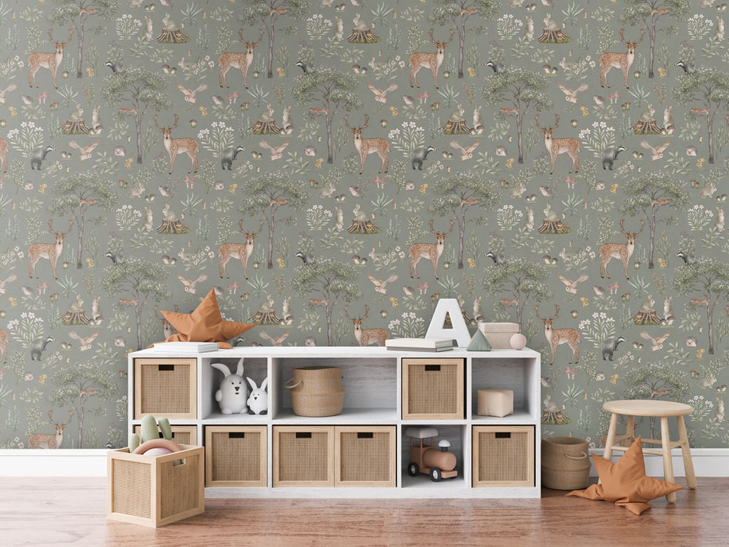 Fantastic Forest, Pattern Wallpaper in green, the room includes a white storage unit with woven baskets, a star-shaped cushion, a letter 'A,' and some books. Additionally, there is a wooden stool with another star-shaped cushion and a basket of toys on the floor. The room has a cozy wooden floor.