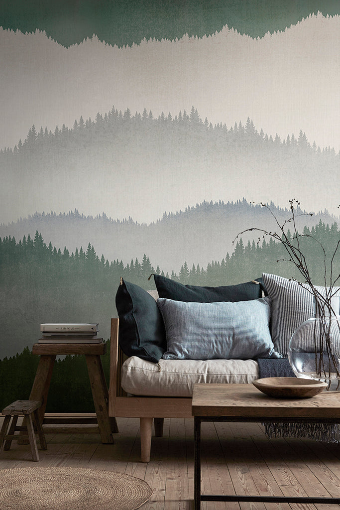 Forest Landscape, Ombre Mural Wallpaper in Dark Green featured in a wall of a living area with wooden furnitures and flooring, with an assortment of pillows on top of a cushion. 