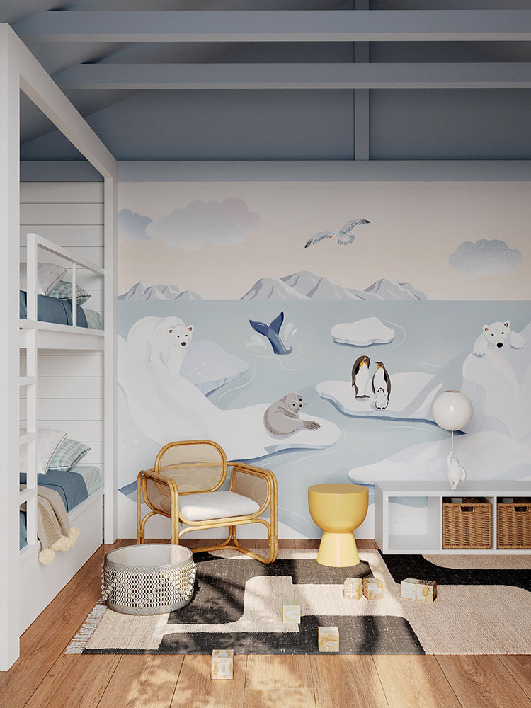 A child’s room with modern decor, featuring a rattan armchair, a bright yellow stool, and white open shelving filled with books and toys. The floor is wooden with a plush rug and scattered toys, creating a playful area. The room is adorned with a whimsical Frosty Friends at the Arctic, Animal Mural Wallpaper.