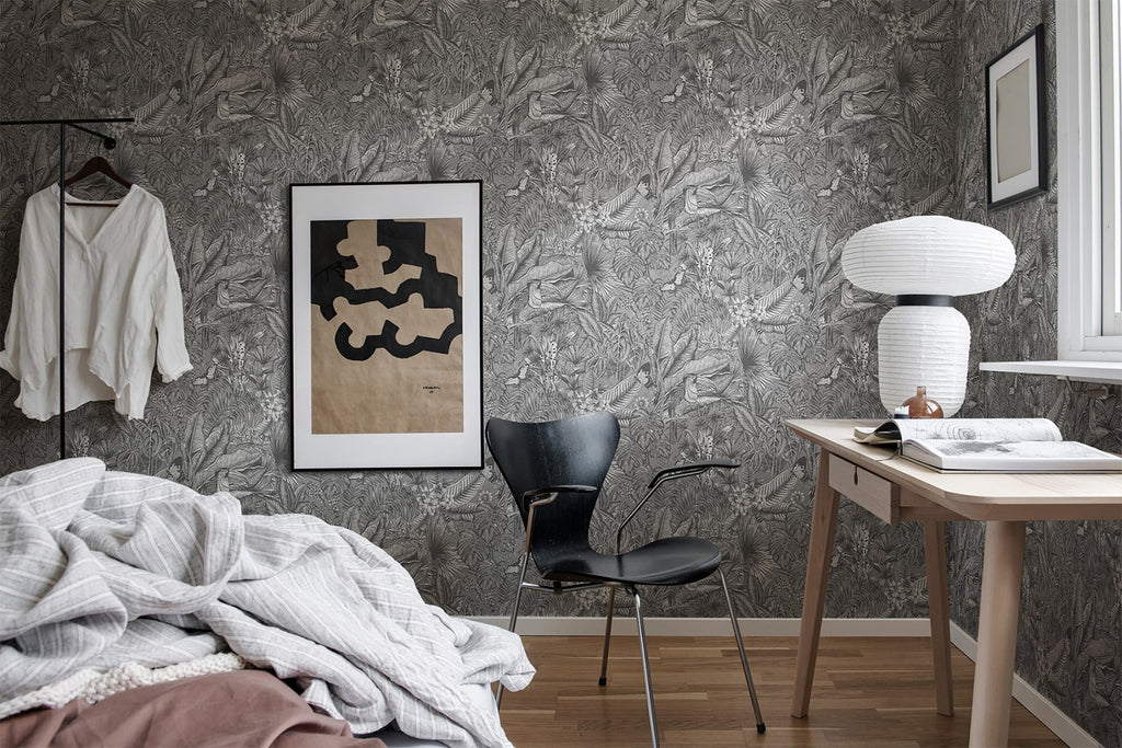 A modern, inviting bedroom featuring a neatly made bed, stylish artwork, and a contemporary desk setup. The room is enhanced by the Furada Floral & Toucan Pattern Wallpaper in Dark Grey, adding a touch of elegance.