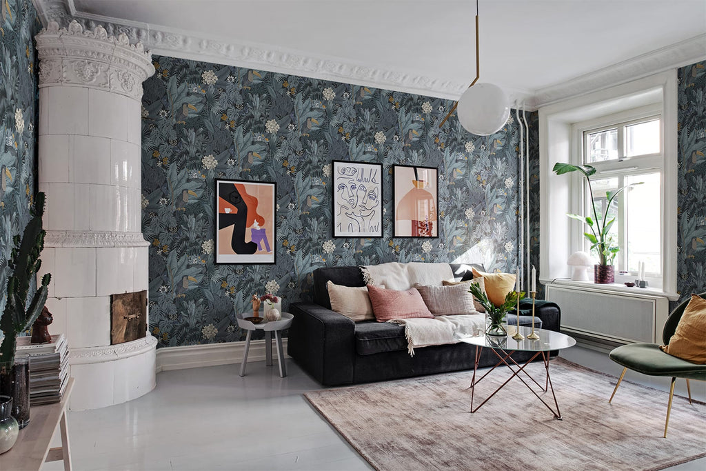A modern living room with Furada Floral & Toucan Pattern Wallpaper in Light Grey, featuring a plush sofa, contemporary art, a classic fireplace, and vibrant indoor plants.
