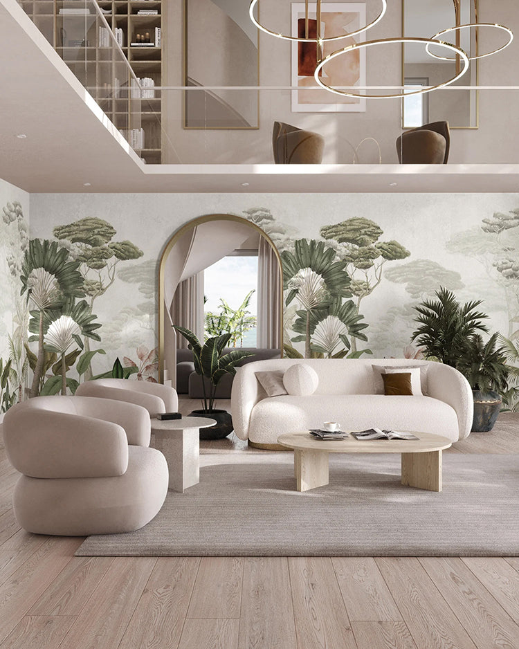 The room features a modern, well-lit living space. The focal point is the Garden Eden, Tropical Mural Wallpaper in White, which showcases greenery and pink flowers. Complementing this naturalistic theme are a beige sofa set, a wooden coffee table, and elegant hanging lights.