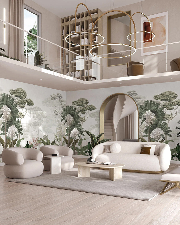 In this spacious, modern living room, natural light floods through tall windows, illuminating a two-level design. The main wall boasts the Garden Eden, Tropical Mural Wallpaper in White,  which transports you to a tropical paradise. The room is furnished with a beige sofa set, a wooden coffee table, and unique circular chandeliers, creating an inviting blend of contemporary aesthetics.
