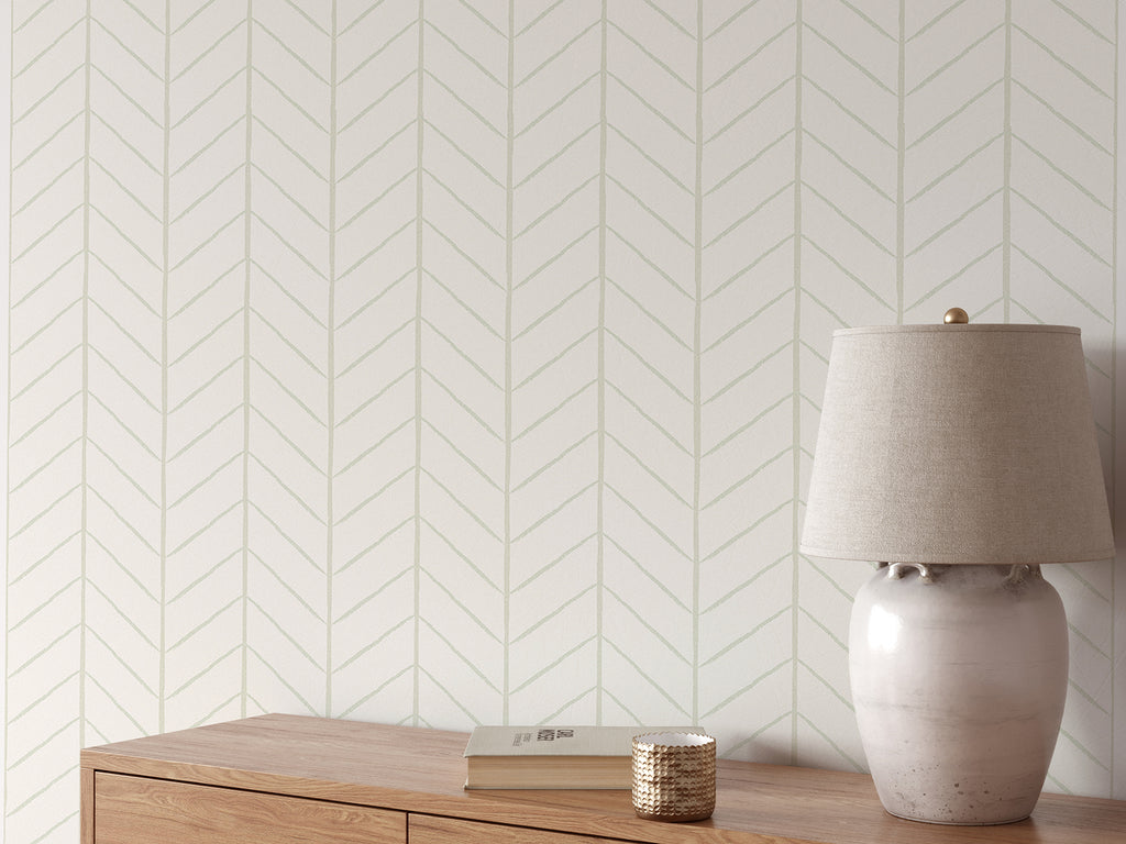 A tranquil room with a wooden sideboard, a ceramic lamp, a book, and a decorative item. The wall is adorned with a subtle Hand-Drawn Herringbone Pattern Wallpaper, creating a warm and serene ambiance.