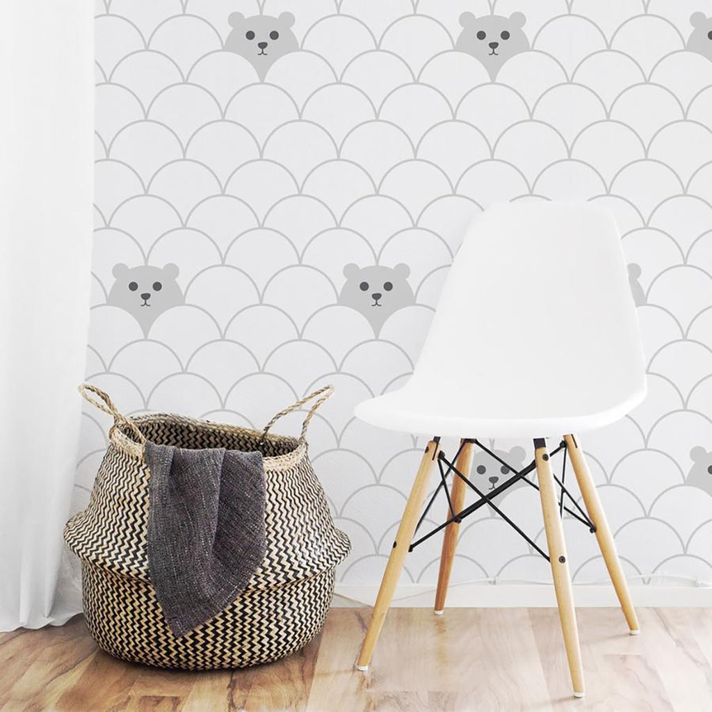 A playful room featuring Hide and Seek Bear, Pattern Wallpaper on a white backdrop. A modern white chair and a woven basket with a grey blanket are in front of the wallpaper. The floor is light-colored wood.