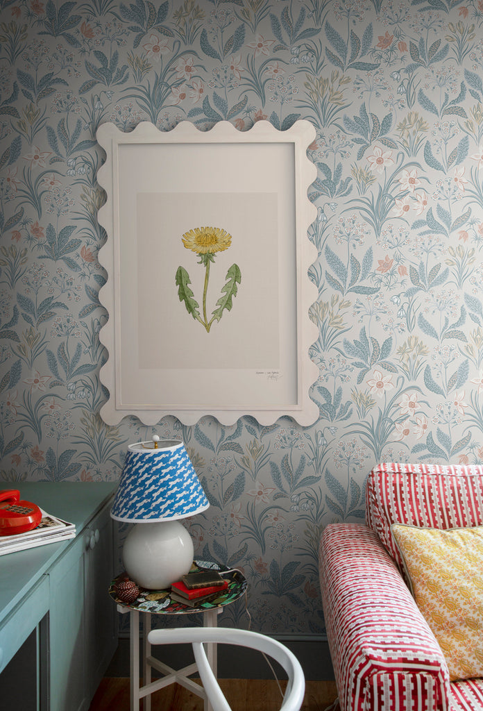 Huset i Solen, Floral Pattern Wallpaper in sand colourway, adorning the wall with a picture frame, featured in a living area with a red and white sofa, and a side table with a lamp.