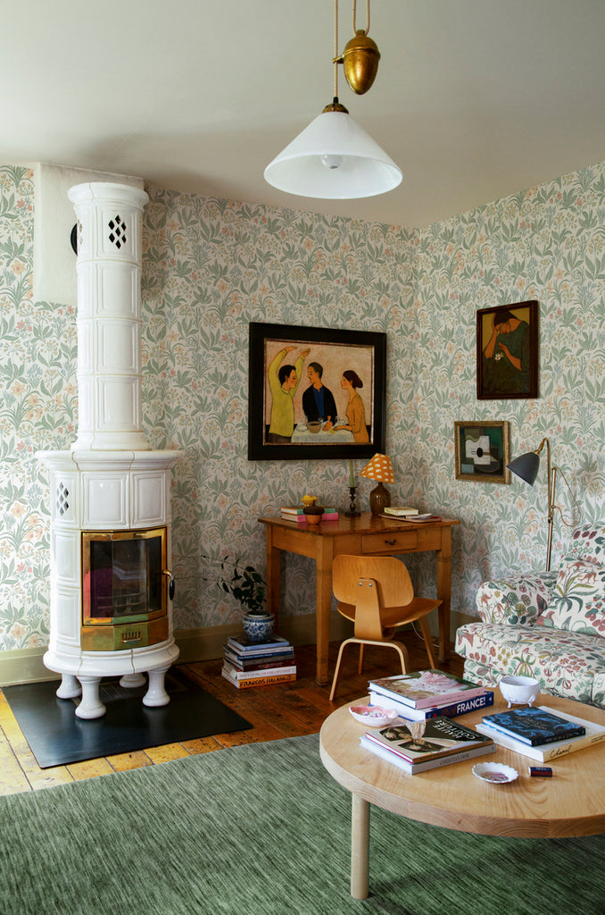 Huset i Solen, Floral Pattern Wallpaper in white  featured in a living area with a wooden table, study table, a green floor mat, and white pendant light. 