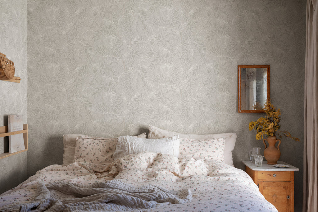 Idun, Nature Pattern Wallpaper in grey featured on a wall of a bedroom with a bed with a patterned sheets and pillows. 