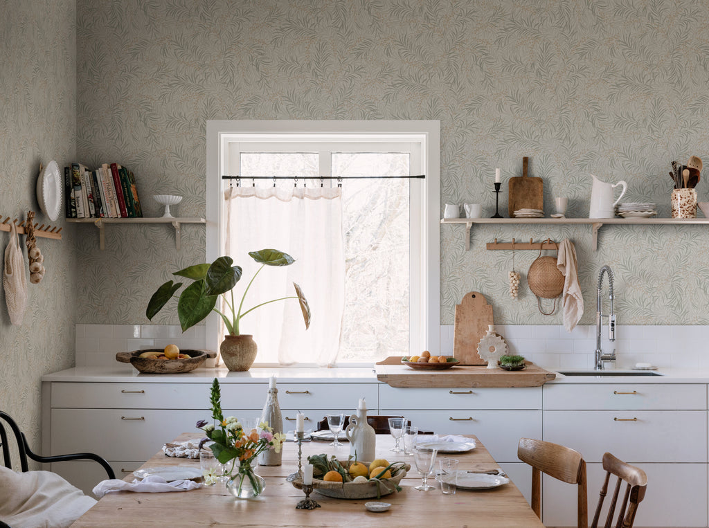 Idun, Nature Pattern Wallpaper in Sand featured on a wall of a kitchen with wooden dining table with kicthen wares on top and a white countertop with foods and planters on it. 