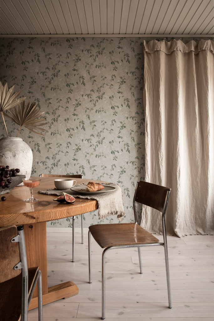 Irene, Floral Pattern Wallpaper in Green featured on a wall a dining area with wooden table and chair with beige curtain on the background