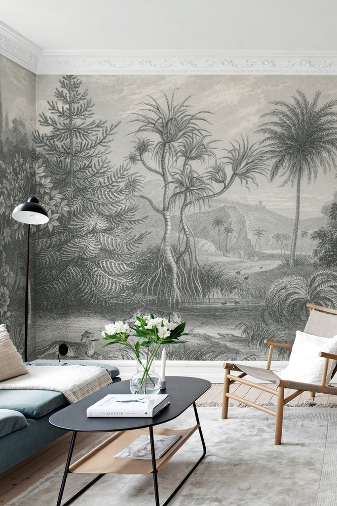 Jungle Land, Mural Wallpaper in dark grey featured on a wall of a living room with black table, rattan chair and a dark blue sofa