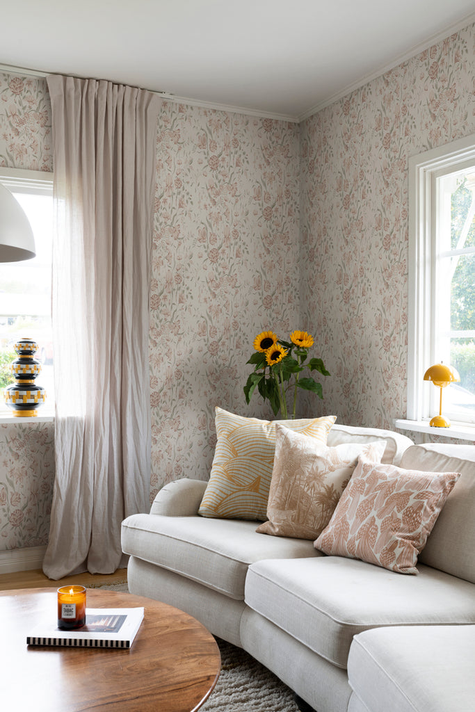 Karins Bukett, Floral Pattern Wallpaper in Sand featured on a wall a living area with white sofa and multicolored pillows, beige curtain, and wooden coffee table