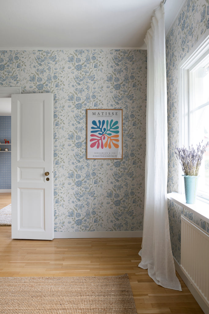 Karins Bukett, Floral Pattern Wallpaper in White featured on a wall an empty room, with a white curtain and a panel window that gives a natural lighting to the room. 