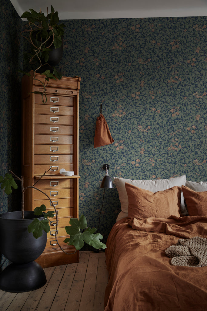 Linnea, Floral Pattern Wallpaper in dark blue featured on a wall of a bedroom with a bed with brown sheets and pillows