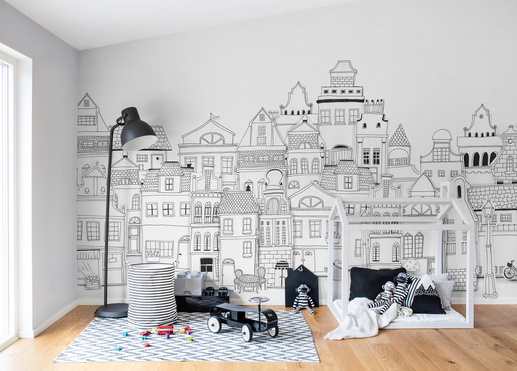 London Houses, Mural Wallpaper in Black White featured on a wall of a kid’s room with several toys scattered and patterned floormat