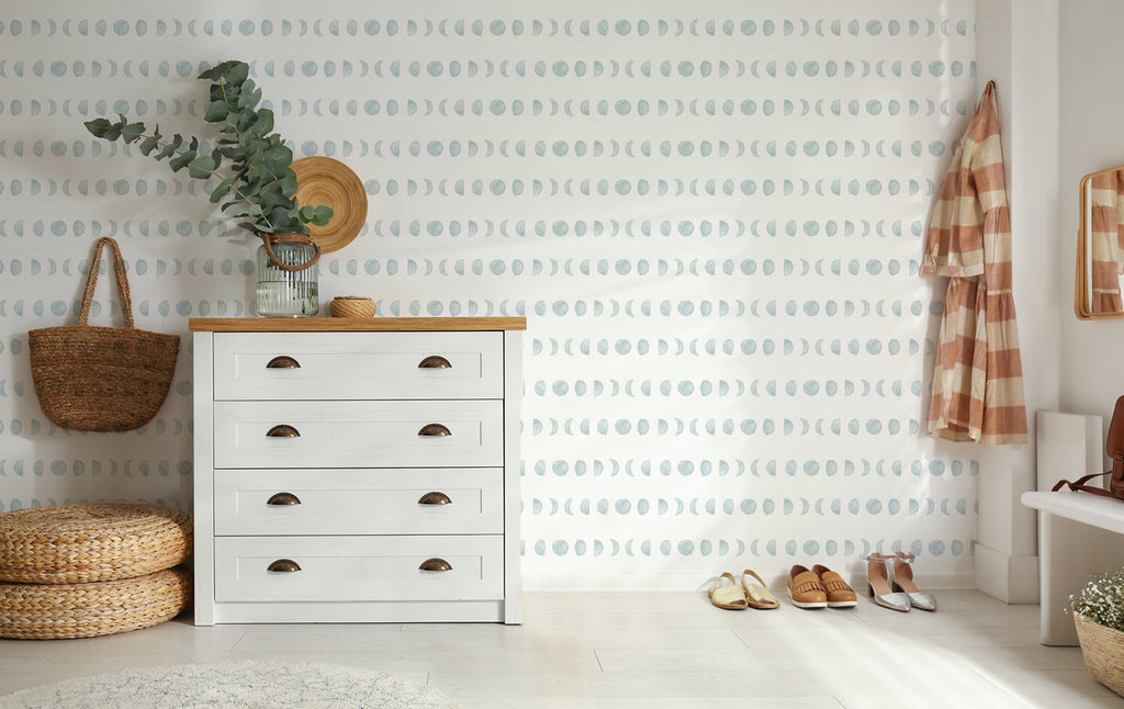 Serene interior featuring Lunar, Pattern Wallpaper with subtle crescent moon shapes. A white dresser, potted plant, woven basket, and straw hat add a natural touch to the modern decor.