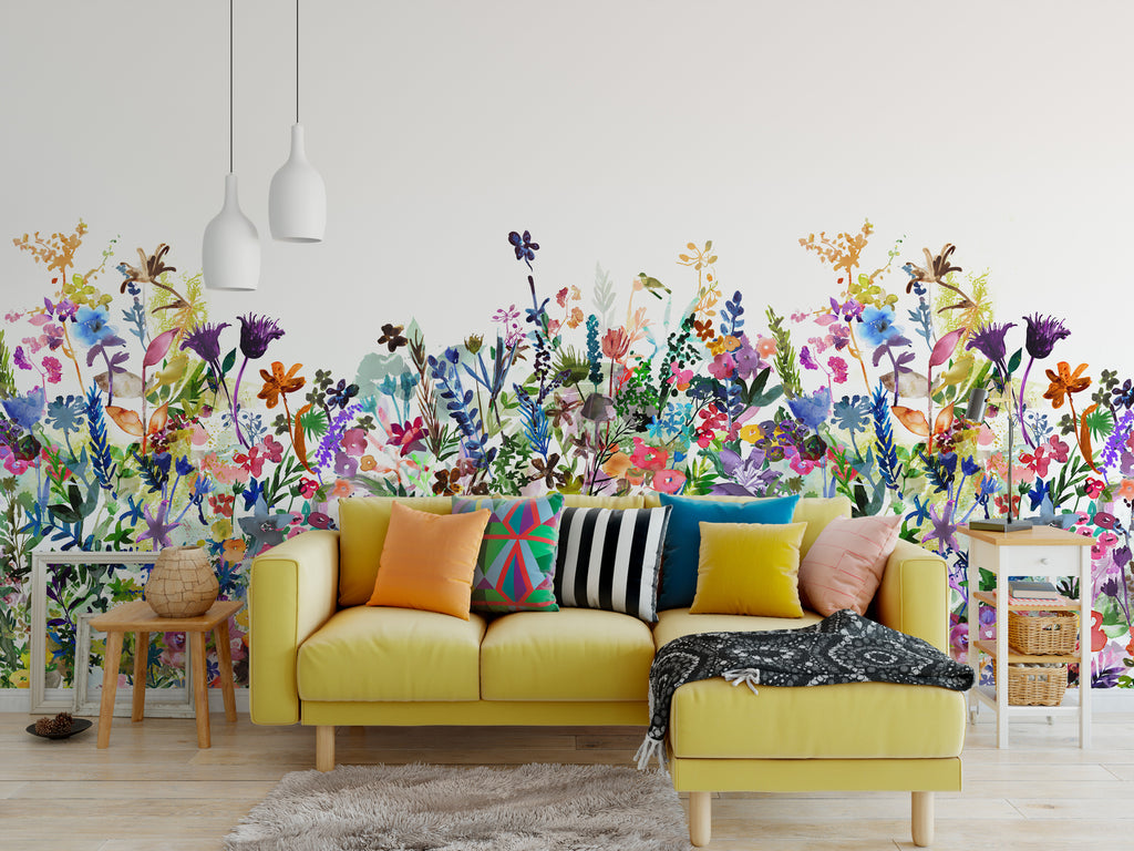 May Meadow, Floral Mural Wallpaper in multicolor bright featured on a wall of a living area with yellow sofa and multicolored pillows