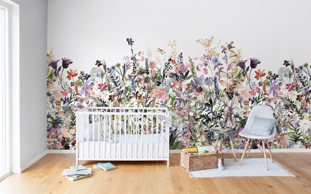 May Meadow, Floral Mural Wallpaper in multicolor pastel featured on a wall of a kid’s bedroom with white crib several scattered items