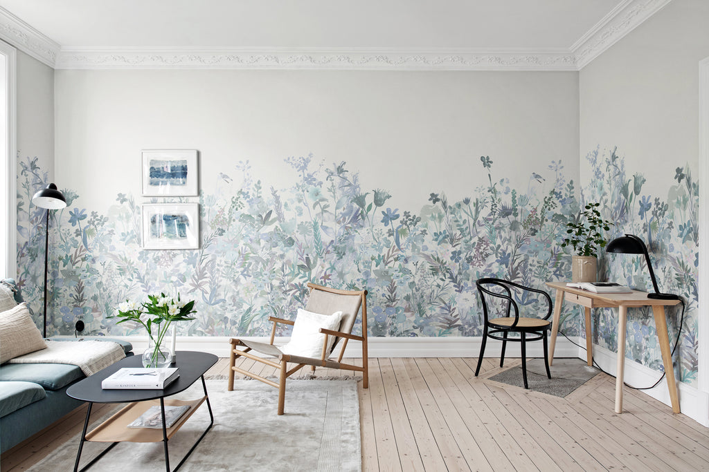May Meadow, Floral Mural Wallpaper in soft blue featured on a wall of a living room with black table, rattan chair and a dark blue sofa