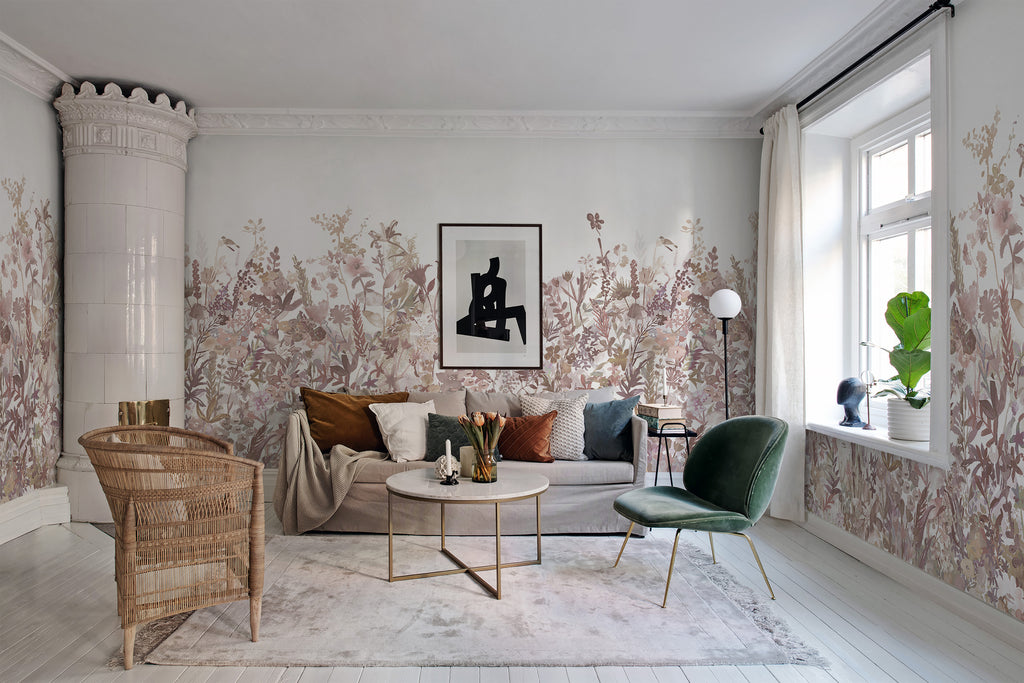 May Meadow, Floral Mural Wallpaper in soft pink featured on a wall of a living room with grey sofa and round table with a rattan chair and a single green sofa chair