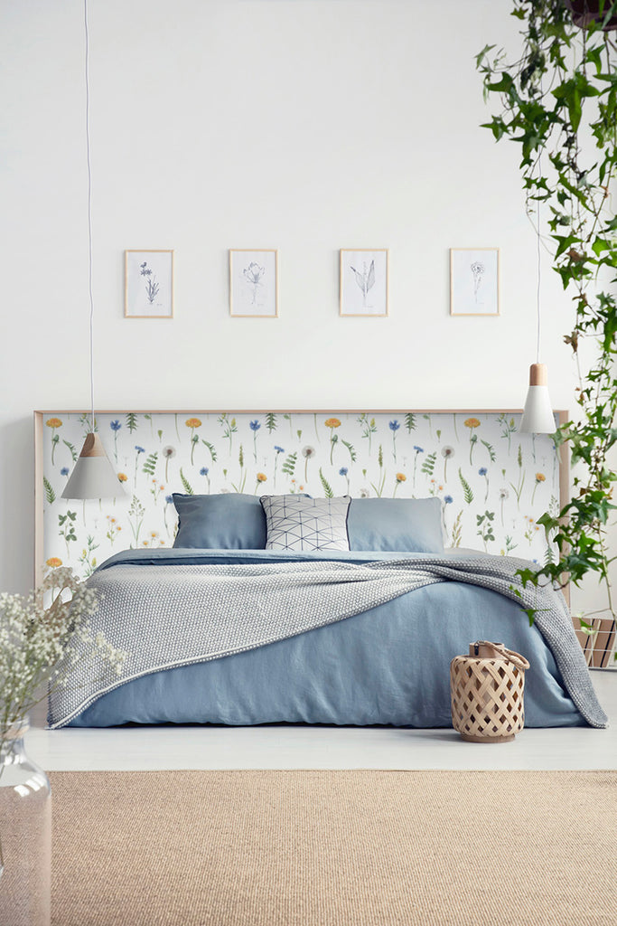 A tranquil bedroom showcasing Meagan, Floral Pattern Wallpaper with subtle botanical motifs. A bed with blue bedding is complemented by framed plant sketches, creating a serene, nature-inspired aesthetic.