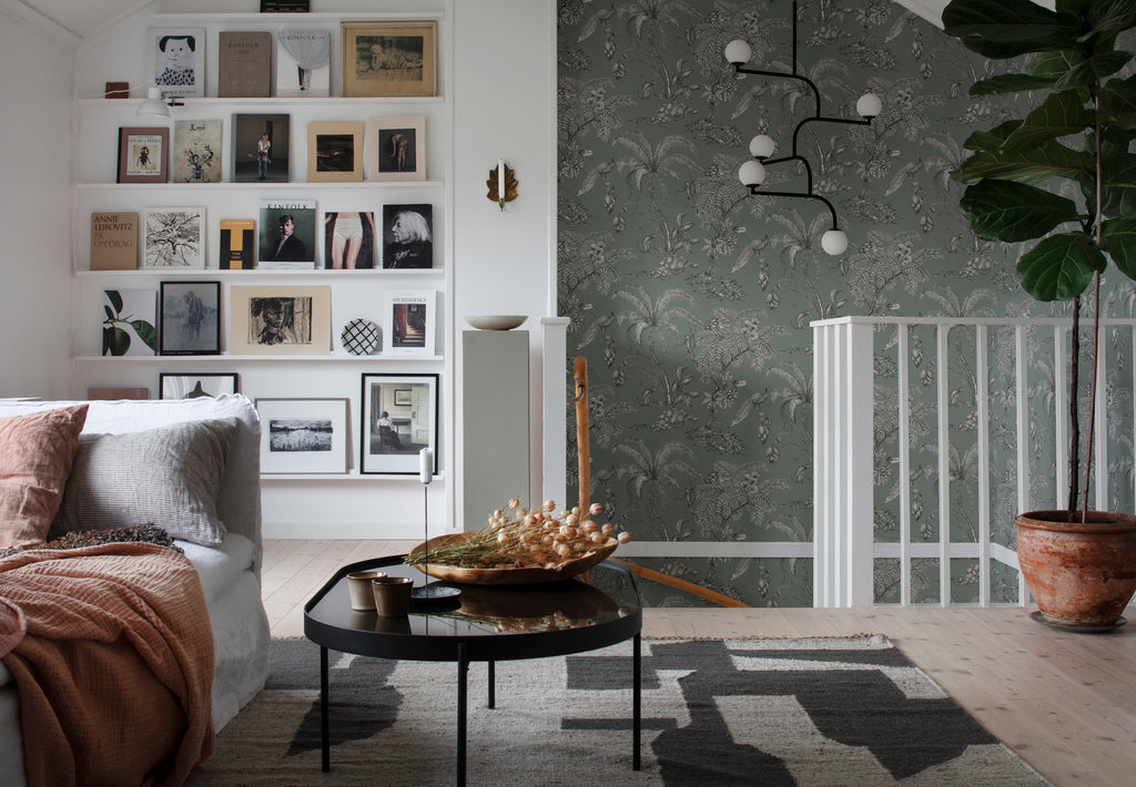 Moa, Tropical Pattern Wallpaper in green featured on a wall of a room upstairs with sofa, coffee table and a side of a wall with full of picture frames