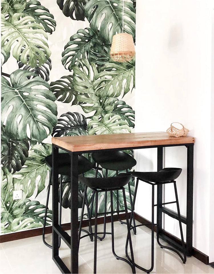 Monstera Green, Tropical Mural Wallpaper featured on a wall of a room with bistro table and chairs with pendant light above it