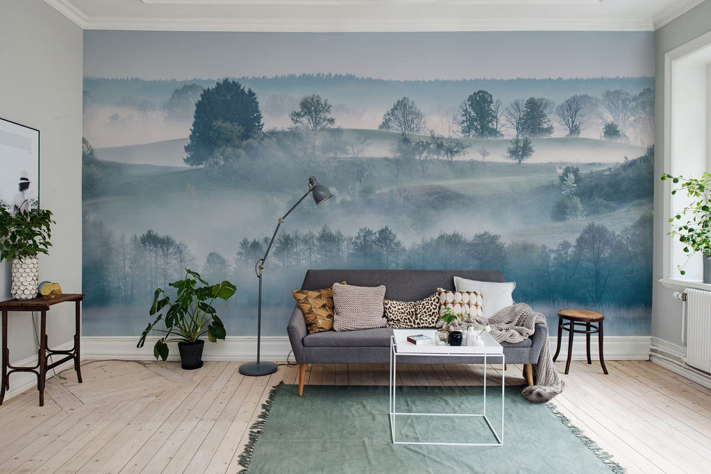 Morning Haze, Blue Landscape Wallpaper featured on wall of a living area with grey sofa that has multiple colored pillows and table