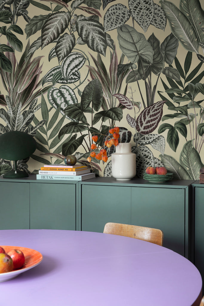Night-time Jungle, Tropical Mural Wallpaper in sand featured on a wall of a room with violet round table and green cabinet with several items on it
