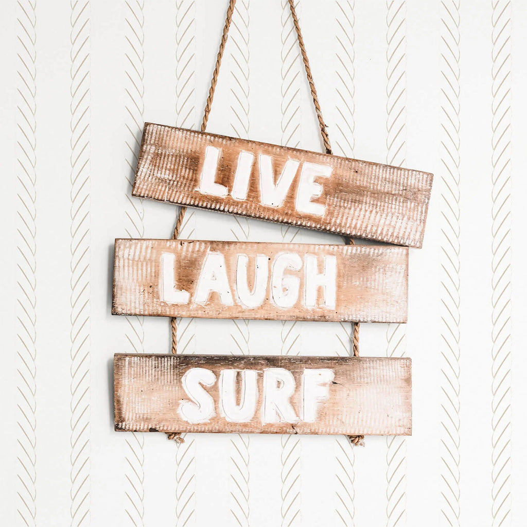 Ocean Rope, Striped Wallpaper depicts three wooden planks, each inscribed with the words “LIVE”, “LAUGH”, and “SURF”. They hang from brown ropes against a backdrop of elegant diagonal stripes. This rustic yet stylish image evokes a sense of coastal living.