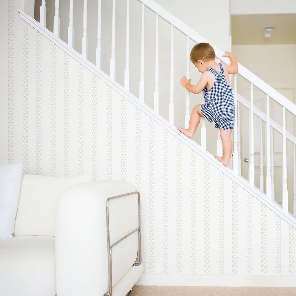 Child ascending a staircase in a bright interior with ‘Ocean Rope, Striped Wallpaper’. The nautical-themed design enhances the modern space, creating a serene, oceanic ambiance.