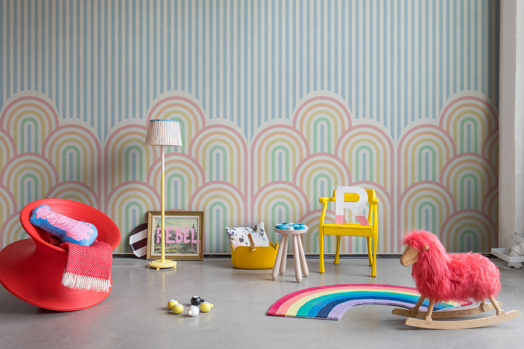 On the Dunes, Geometric Wallpaper in multicolor featured on a kids’ bed room with several scattered toys and rainbow floor mat