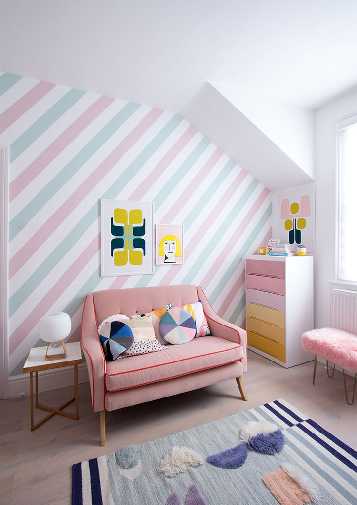 A vibrant attic room with a coral sofa, Pastel Candy Stripes, Wallpaper, colorful throw pillows, contemporary art, a multicolored chest of drawers, and playful area rugs.