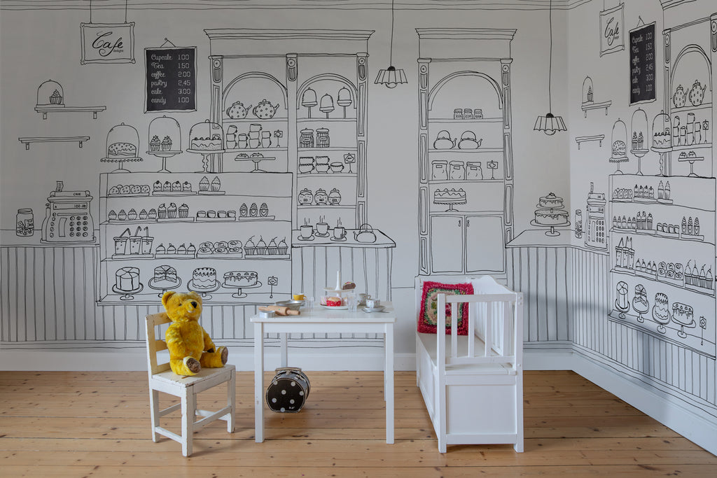 Petite Bakery, Mural Wallpaper as seen on the wall of a child’s playroom with white mini furniture set that has toys on it