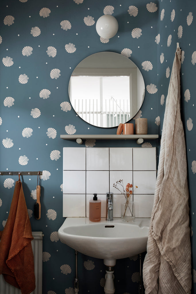 Picking Seashells, Wallpaper in Blue Featured on a wall of a toilet, with a round mirror and a lavatory with several products on top of it
