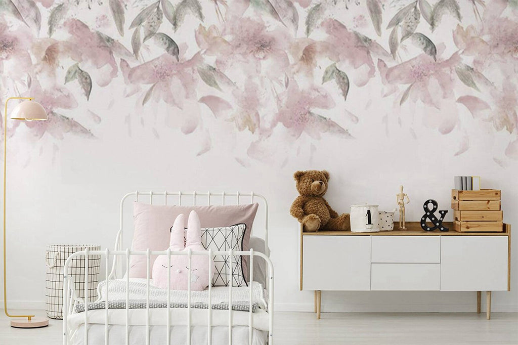 The Pink Florals, Watercolour Mural Wallpaper, enhances a kid’s bedroom that houses a single bed with a rabbit pillow, and a modern white table adorned with a stuffed toy and children’s playthings.