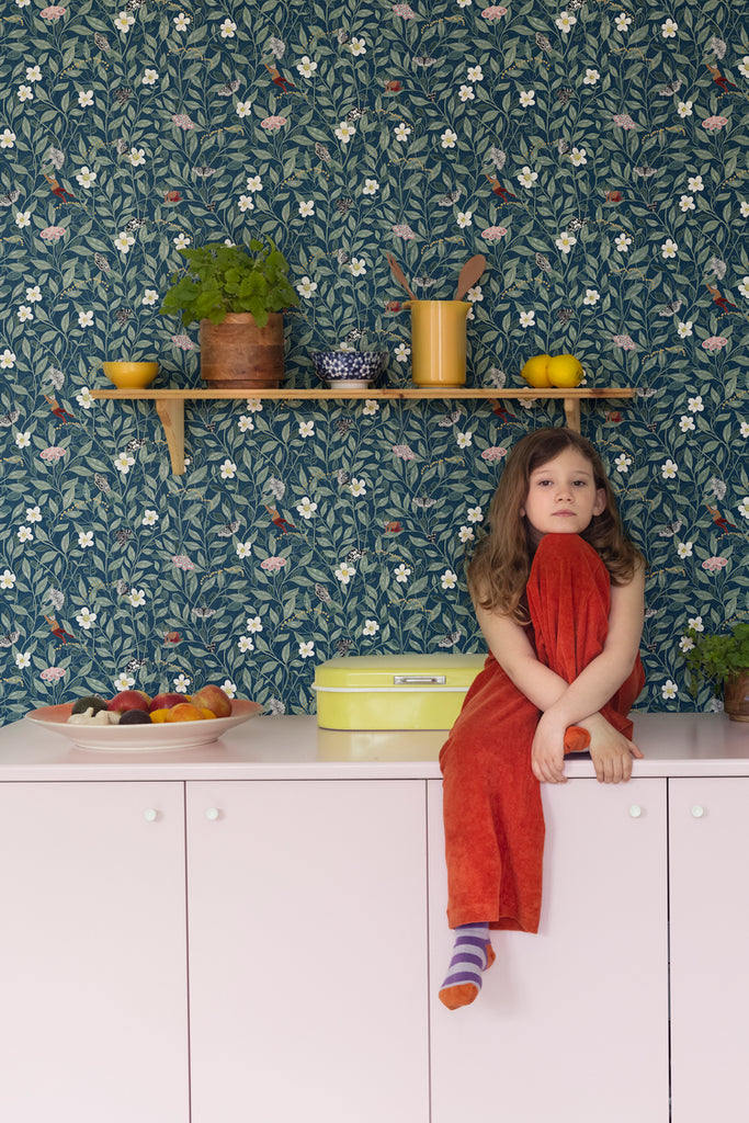 Pixie, Floral Pattern Wallpaper, in dark blue, in the kitchen area with a girl sitting on the cabinet