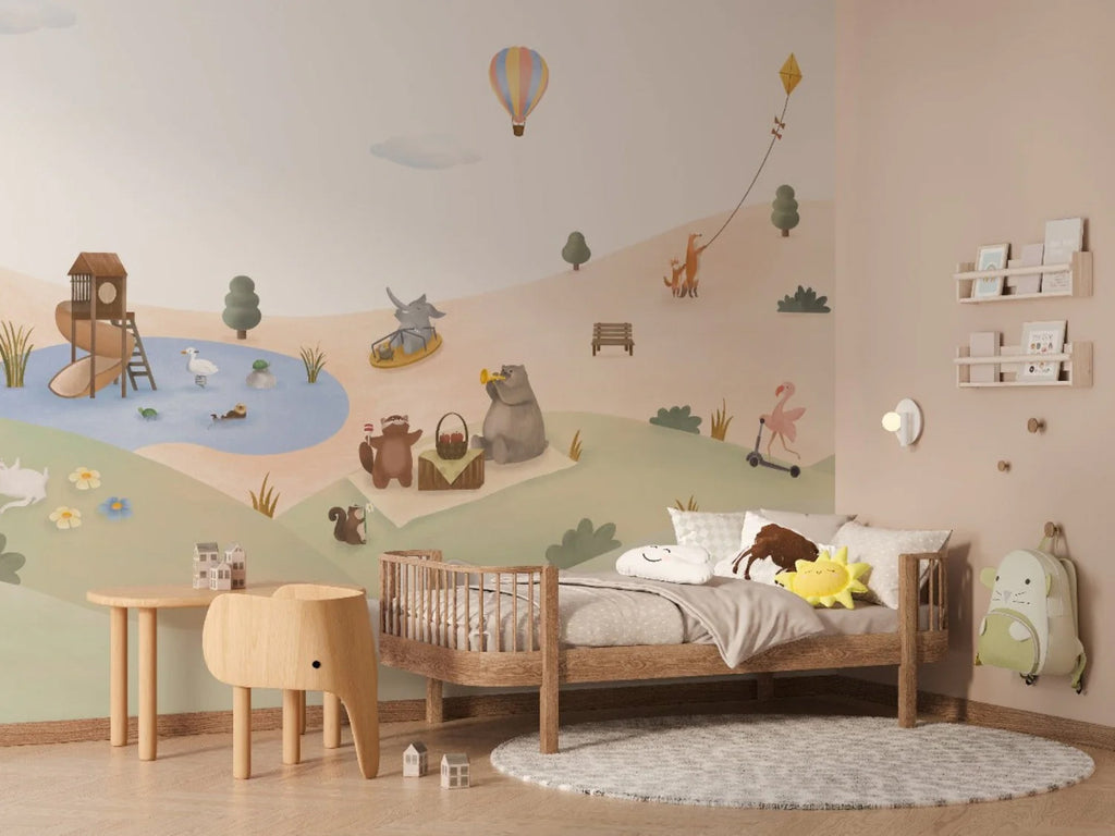 A child’s room with Playground Adventures, Animal Mural Wallpaper on one wall. A wooden crib with plush toys, a small white shelf with books, a grey rug, and a green backpack on the wall.
