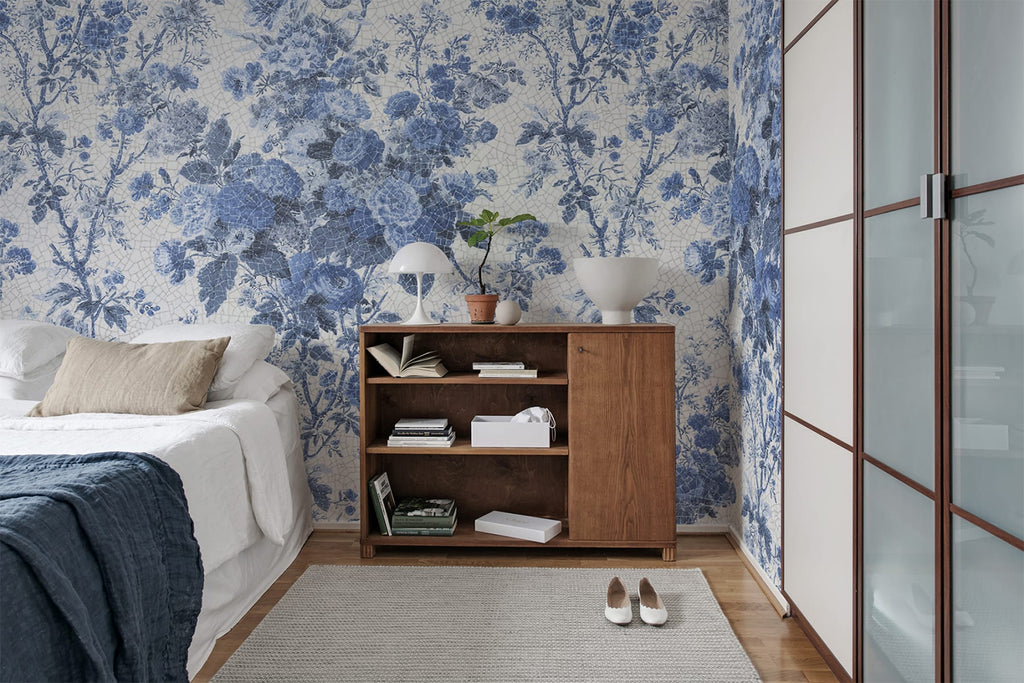 Porcelain, Floral Pattern Wallpaper in blue featured on a wall of bedroom with a bed that has white sheets and blue throw blanket and a wooden bedside storage 