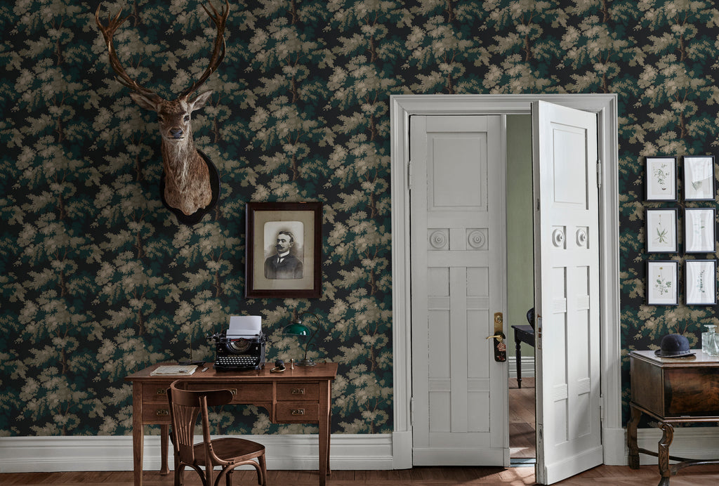 Raphael Floral, Wallpaper in Dark Green featured on a wall of a room with a wooden table that has a vintage typewriter, a chair, and a white door.