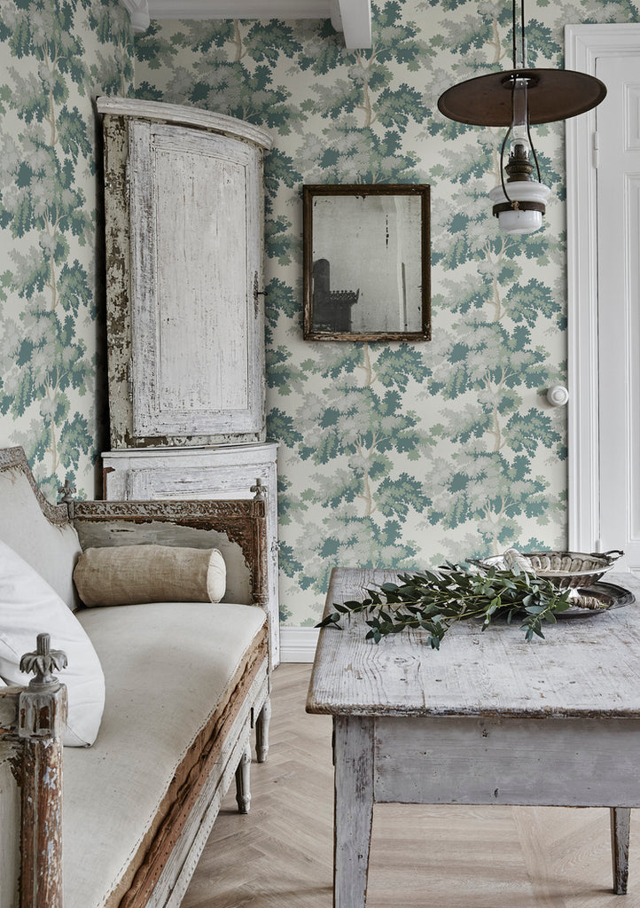 Raphael Floral, Wallpaper in Light Green featured on a wall of a room with a worn out white table and vintage chair and a light wood flooring