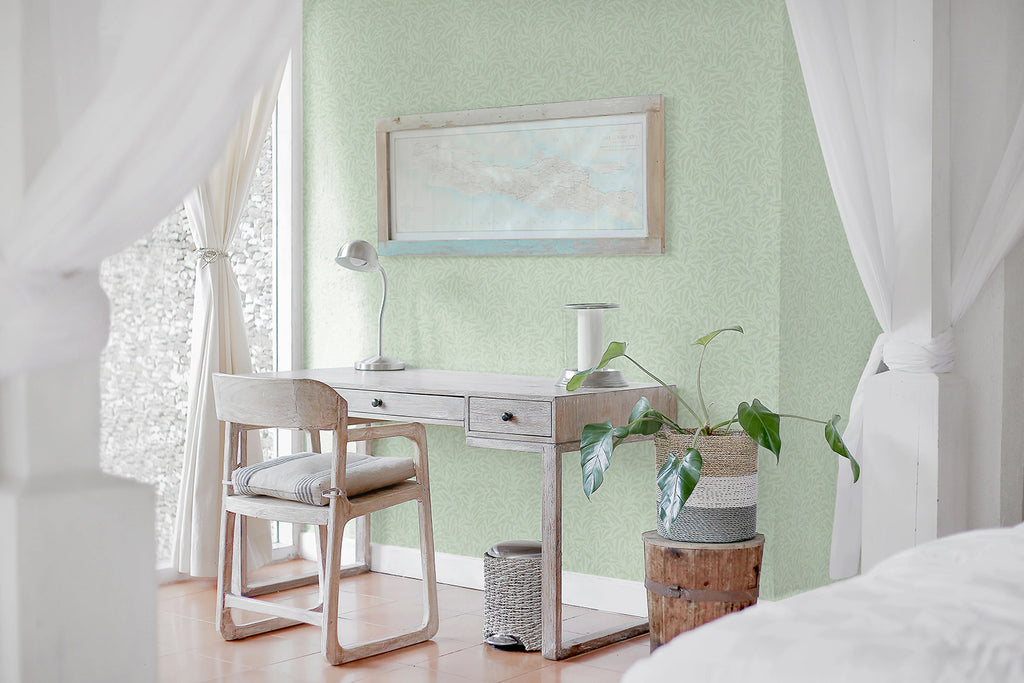 A bright, airy room with a white desk and chair. Natural light filters through sheer curtains. Indoor plants add life to the space. The wall features a calming Rippling Leaves pattern wallpaper in Sage.