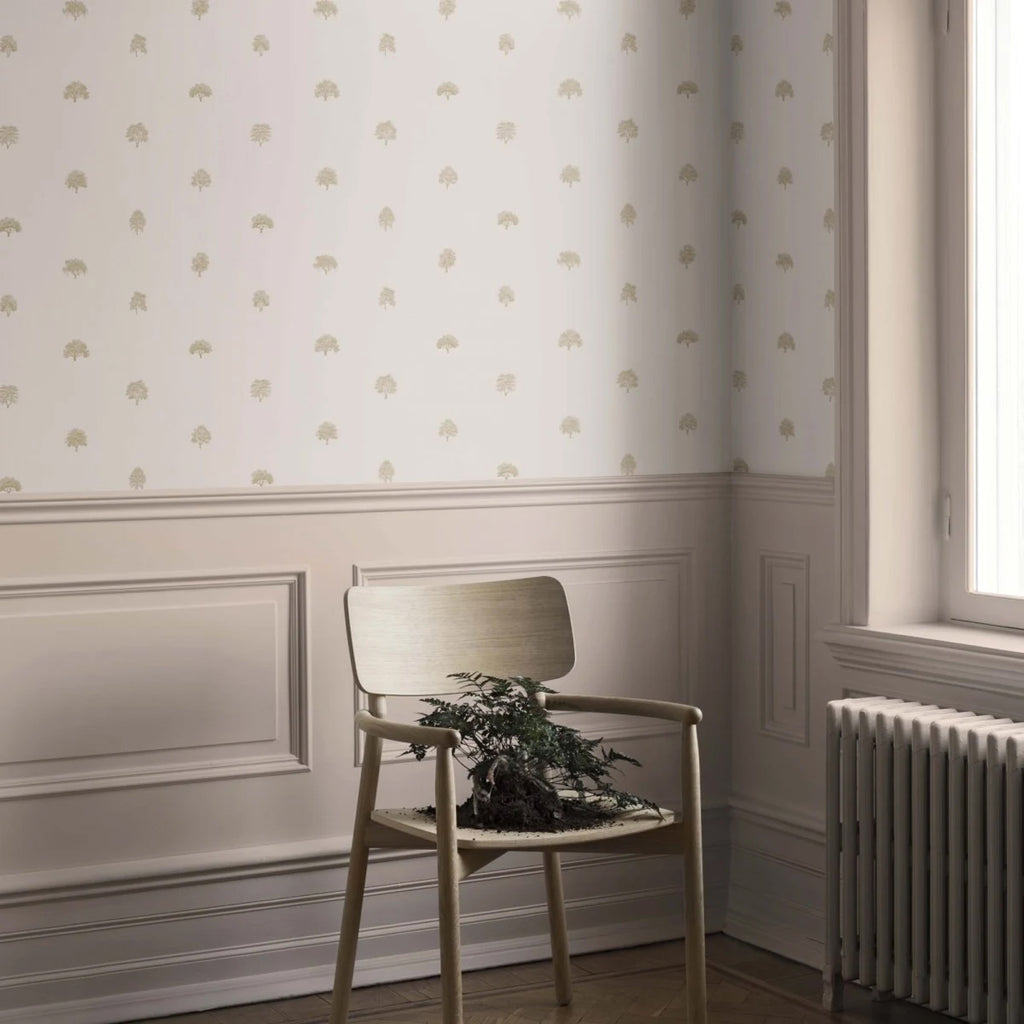Rowena Trees Patterned Wallpaper in blush pink featured on a wall of a room with single wooden chair adjacent to a window