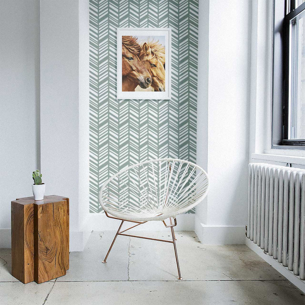 A cozy corner with Sage Layered Herringbone Pattern Wallpaper. A white modern chair, wooden cube table with a green plant, and a framed horse portrait add to the room’s decor.