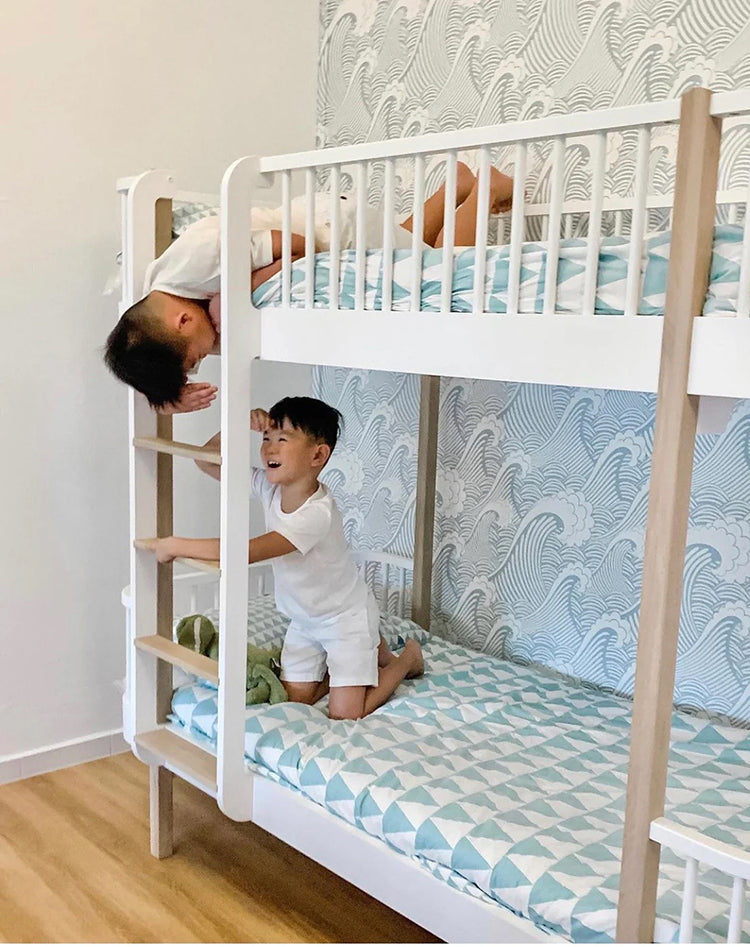 A lively children’s bedroom featuring Sail Away, Blue Pattern Wallpaper with a nautical theme. White bunk beds are occupied by two children, one climbing the ladder and another on the lower bunk.
