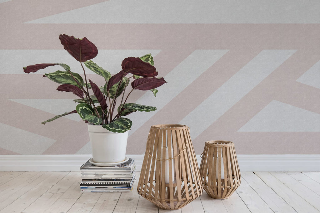 Sailor's Sea, Striped Wallpaper in Blush Pink  Colourway featured on a wall of a room with wooden candle holder, and stacked books with plant vase, with wooden flooring